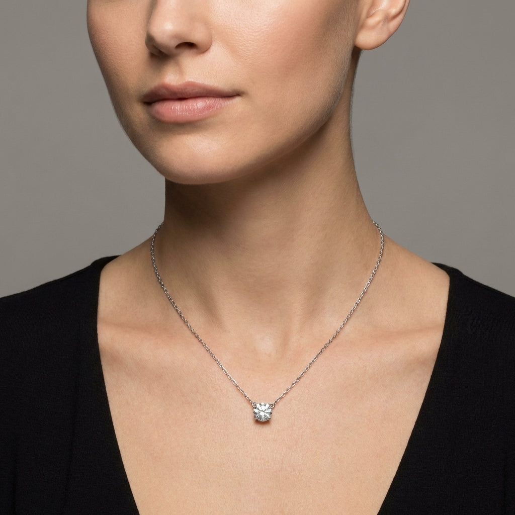 Close-up of a person wearing a silver necklace with a square pendant on a neutral background