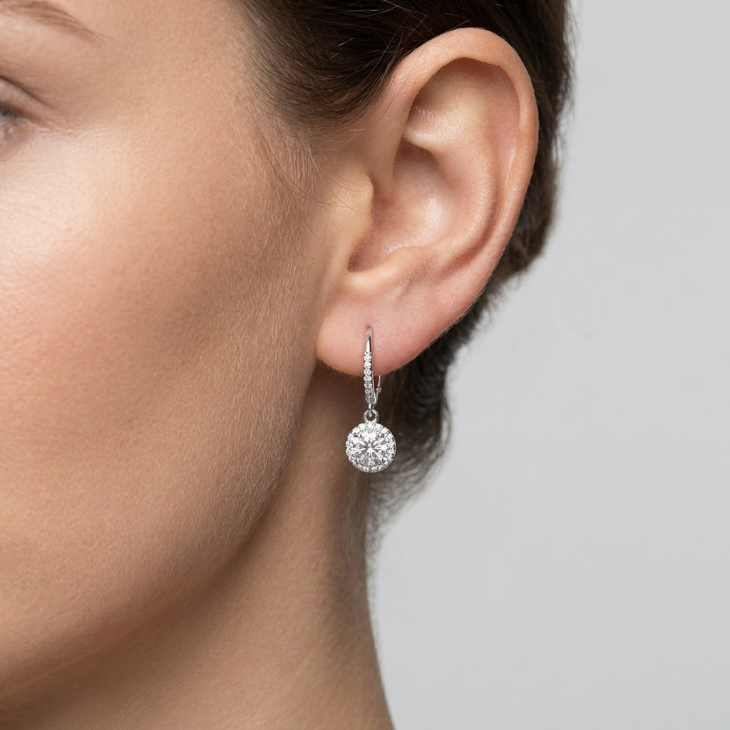 Close-up of a woman wearing a silver earring with a clear gemstone on a neutral background