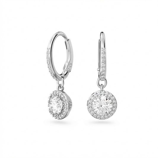 lean white or soft pastel background — the Swarovski Una Angelic crystal drop earrings displayed side by side on a flat surface or earring stand. The angel wing design catches soft light, showcasing Swarovski's signature brilliance, the delicate wing silhouette, and the graceful drop chain.