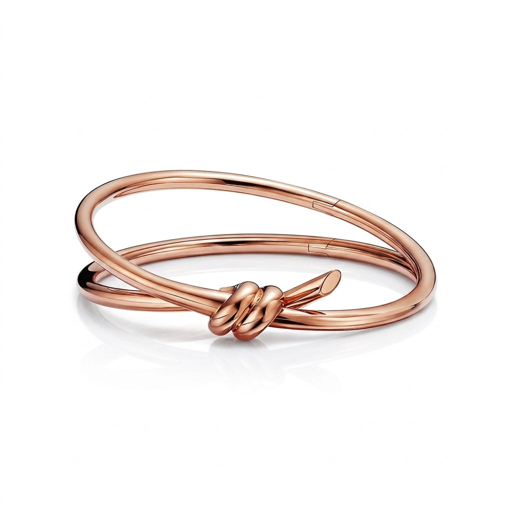 A polished rose gold bangle bracelet with a knotted detail at the center, displayed on a clean white background with a soft reflection.
