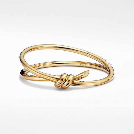 A polished yellow gold bangle bracelet with a knotted ribbon detail at the center, displayed on a clean white background.