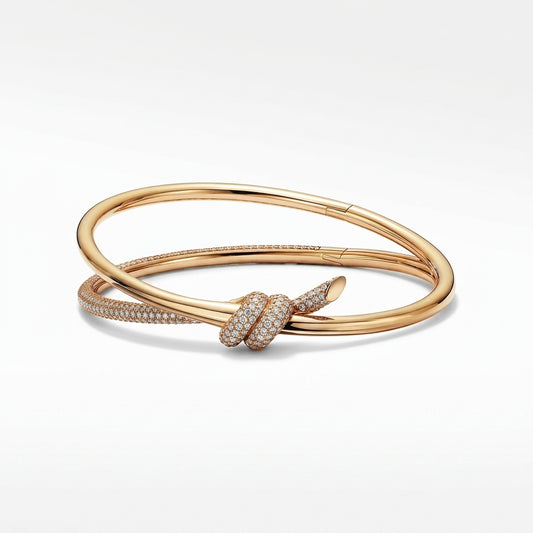 A gold bangle bracelet with a knotted design, featuring a pavé diamond-encrusted center knot and a row of small pavé diamonds along one arm, shown on a clean white background.