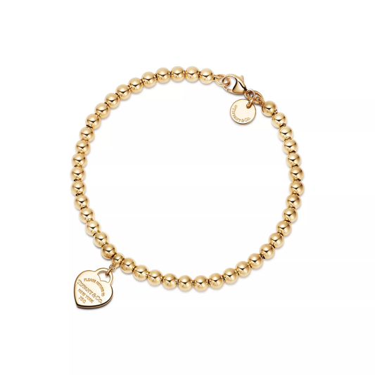 Gold beaded bracelet with a heart-shaped tag on a white background