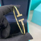 Gold bracelet with letter 'T' design held by a black glove against a blue background