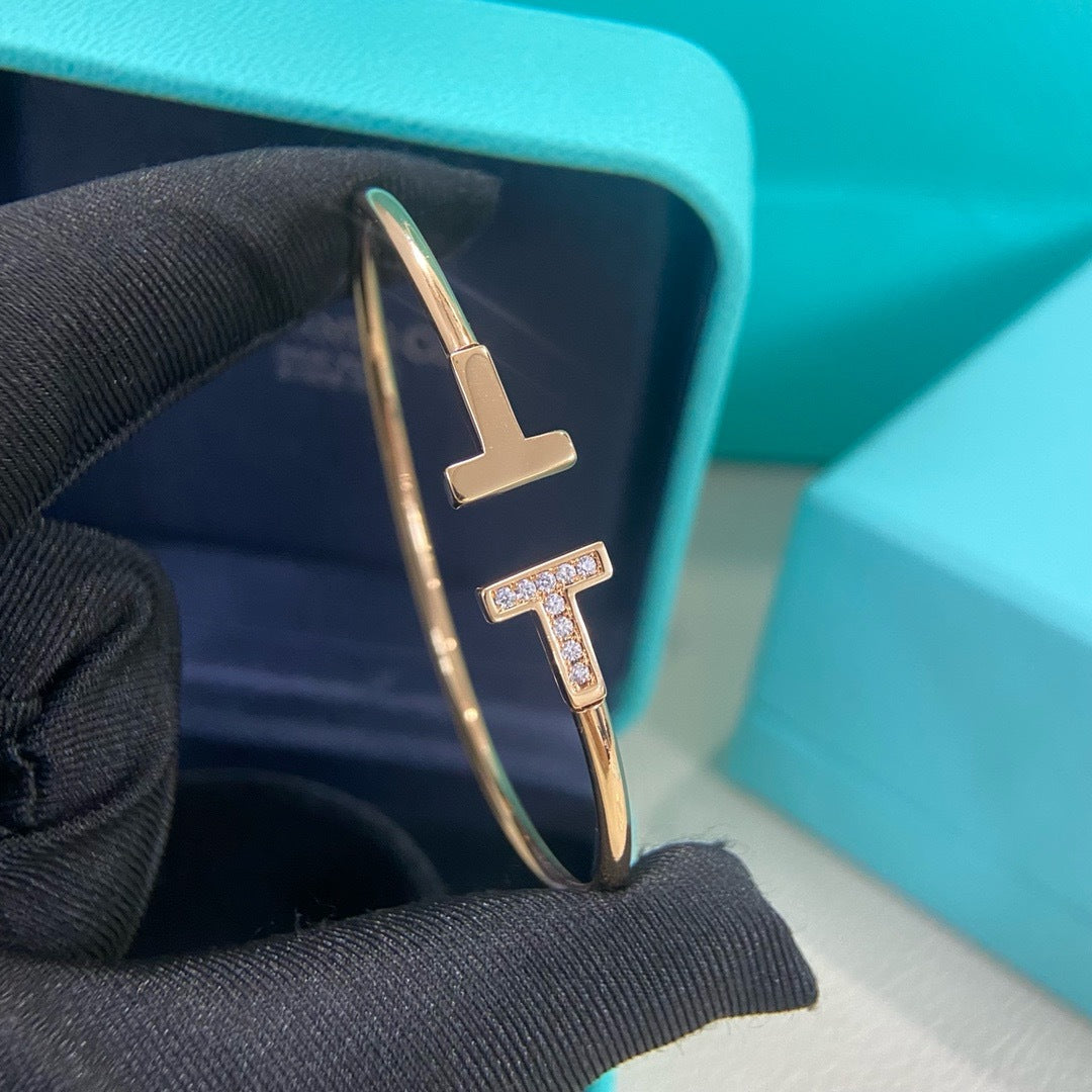 Gold bracelet with 'TT' design on a black fabric background