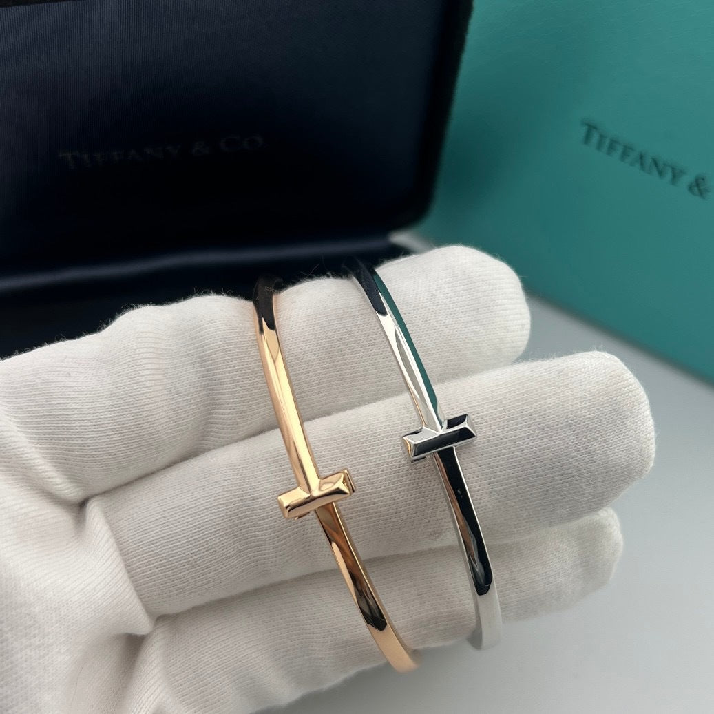 Gold and silver cross-shaped earrings on a white cloth with Tiffany & Co. branding in the background.