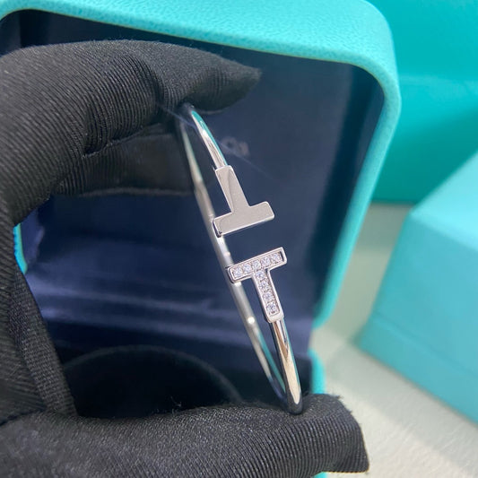 Silver cross-shaped earring held by a black-gloved hand against a teal background