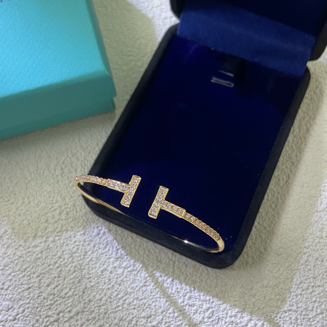 Gold 'H' shaped earring in a blue jewelry box on a textured surface.