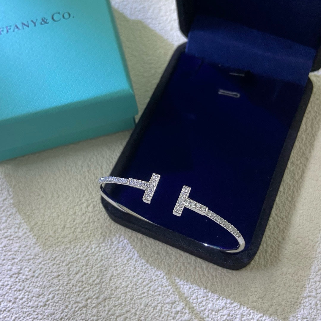 Silver bracelet with 'T' design on a blue jewelry box with Tiffany & Co. branding.