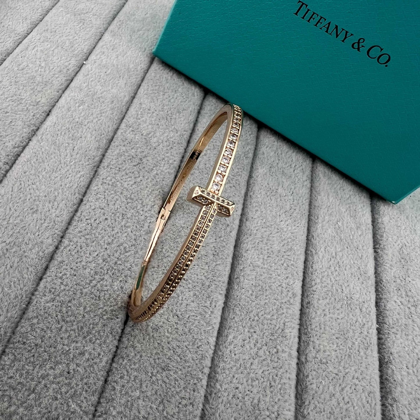 Gold bracelet on a textured surface with a Tiffany & Co. box in the background