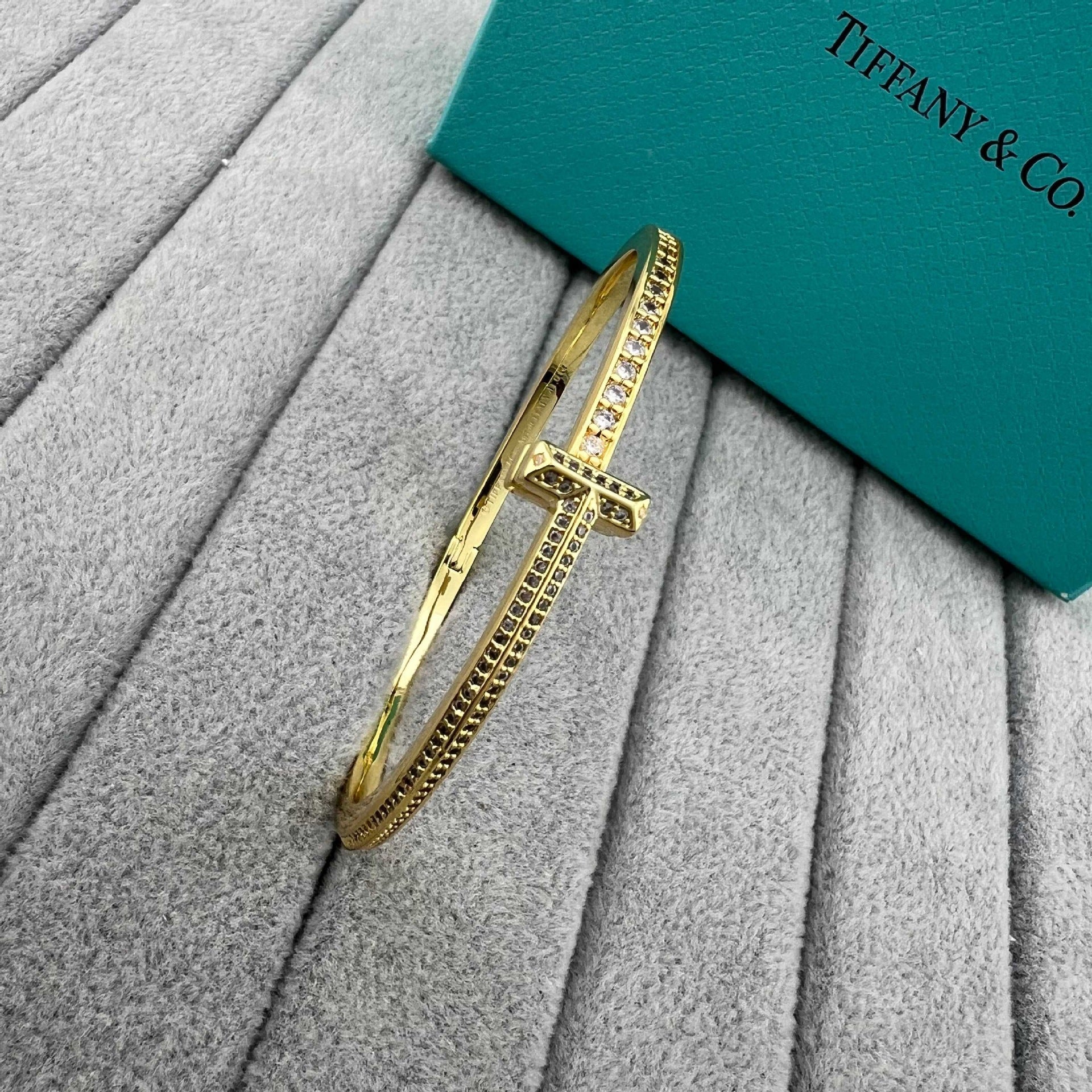 Gold bracelet on a textured surface with a Tiffany & Co. box in the background
