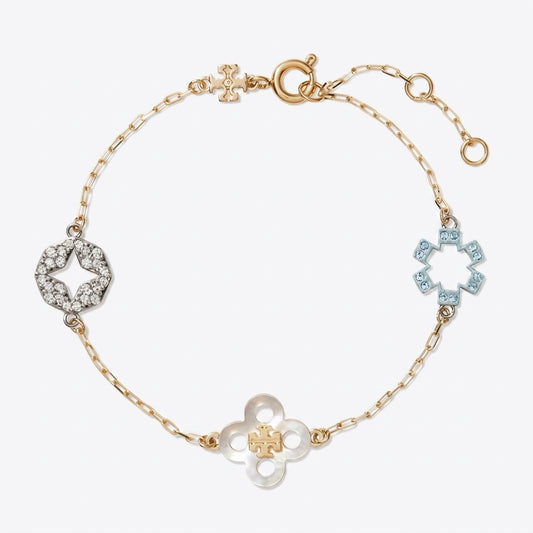 A delicate gold chain bracelet featuring three distinct flower-shaped charms: a central gold clover with a small gold cross in the center, a left-side silver star-shaped charm paved with clear stones, and a right-side light blue star-shaped charm paved with blue stones. The bracelet is displayed on a clean, light gray background.