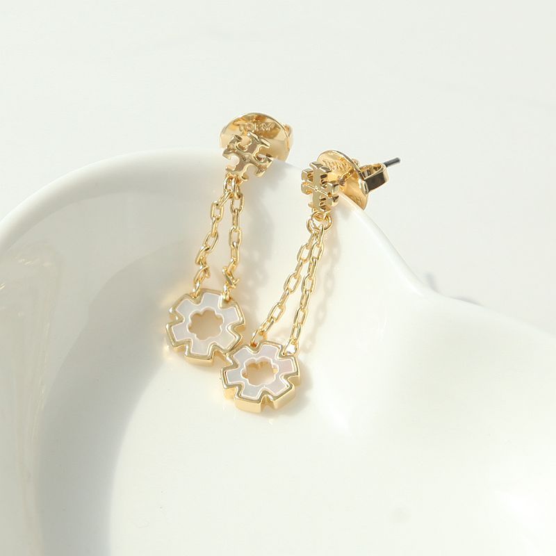 A pair of gold dangle earrings with white inlay clover motifs, resting on a white ceramic dish against a white background.