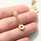 A gold-tone dangle earring with a circular logo stud, delicate chain, and a flower-shaped drop charm, shown resting on a person's fingers.