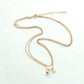 A delicate gold chain necklace with a small dangling charm and a tiny clover-shaped accent, displayed on a clean white background.