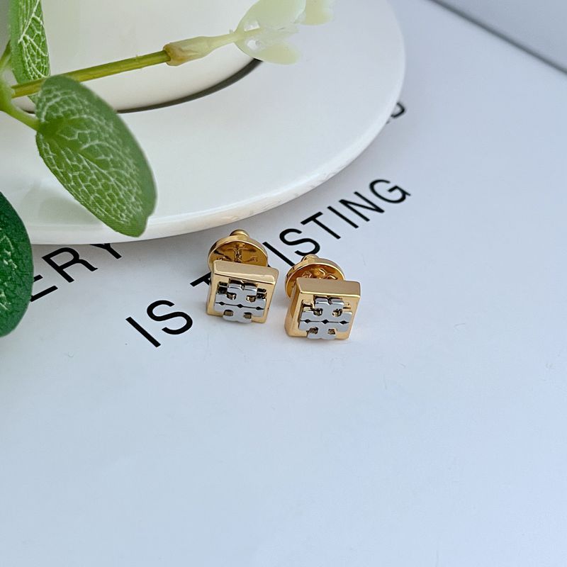 Clean, angled shot of a single stud against a solid dark background, dramatically highlighting the contrasting silver and gold tones and the sharp, geometric lines of the block logo.