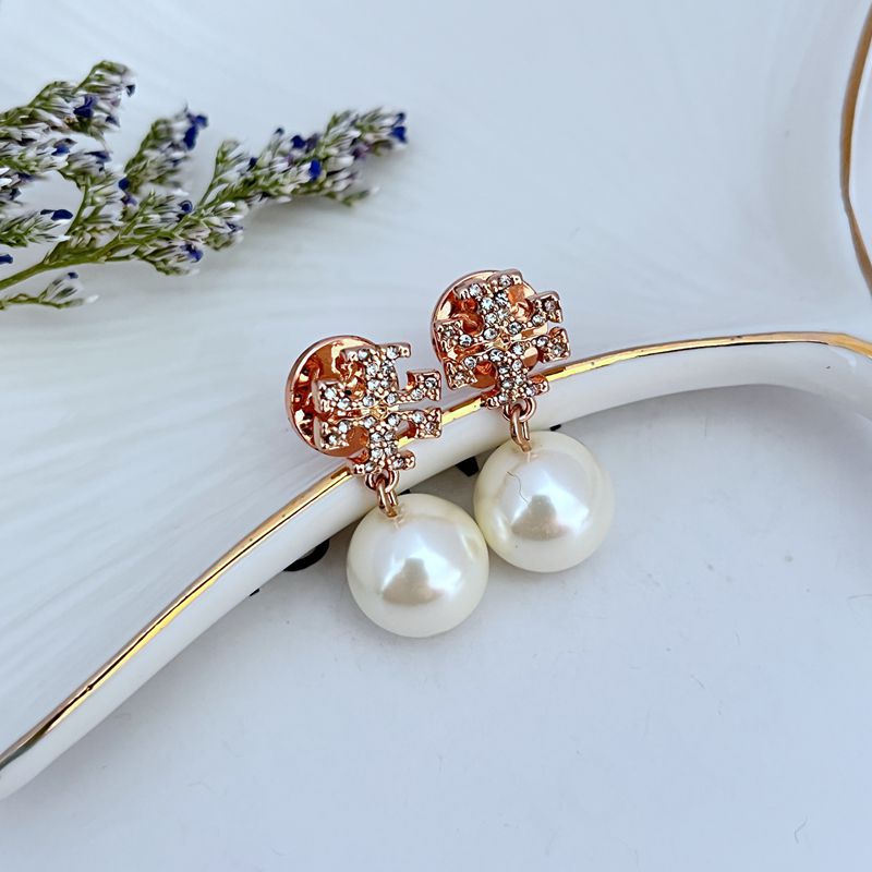 Clean, front-facing shot of a single earring against a soft, neutral background, showcasing the Double T logo above the pearl drop.