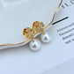 Clean, front-facing shot of a single earring against a soft, neutral background, showcasing the Double T logo above the pearl drop.