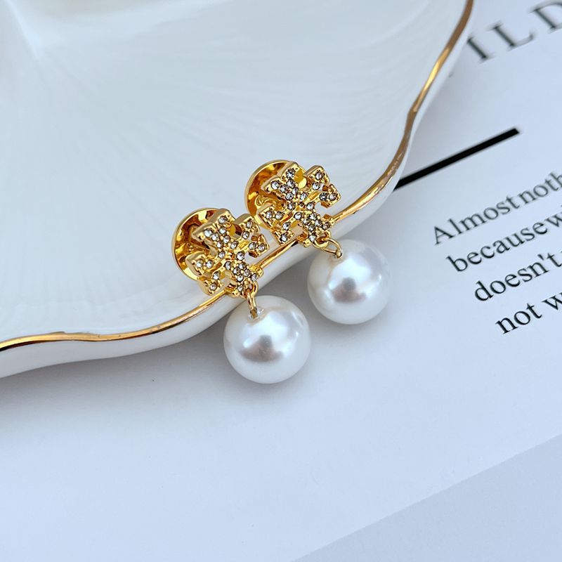 Clean, front-facing shot of a single earring against a soft, neutral background, showcasing the Double T logo above the pearl drop.