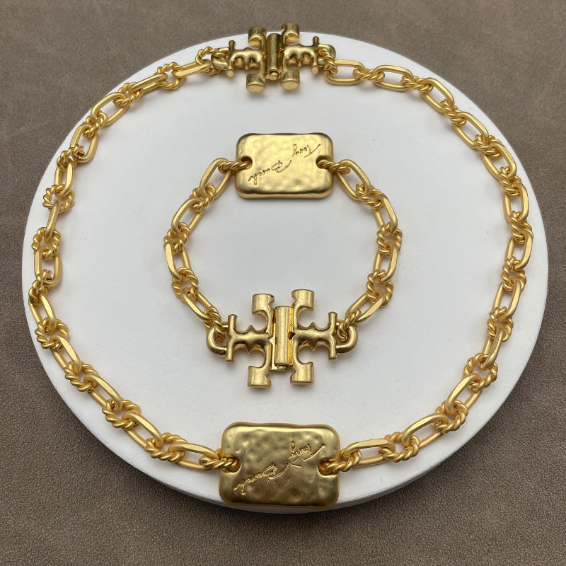 A flat lay or styled shot featuring 2-3 different chunky Tory Burch necklaces (e.g., a resin link chain, a large pendant piece, and a mixed-metal design) arranged on a neutral background.