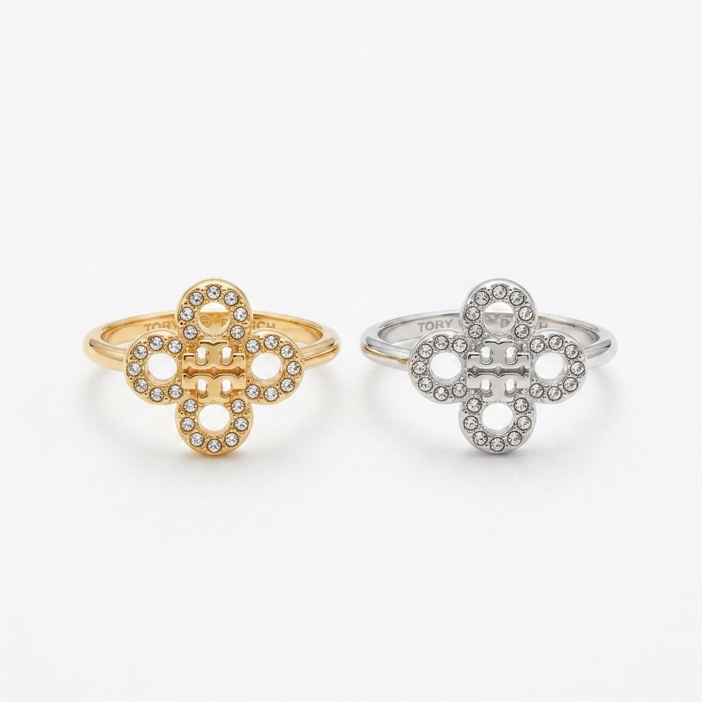 Two interlocking clover-shaped rings, one in yellow gold and one in silver, both adorned with small clear stones, shown on a plain light gray background.