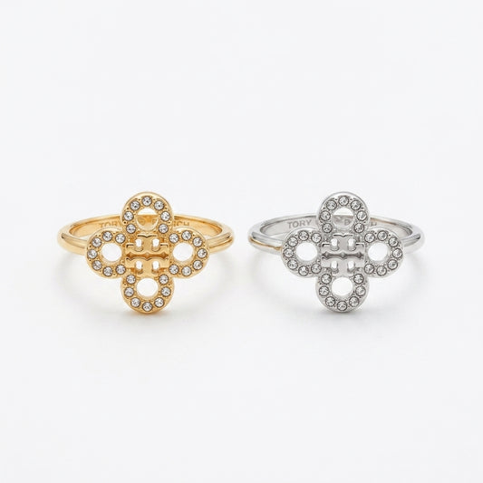 Two interlocking clover-shaped rings, one in yellow gold and one in silver, both adorned with small clear stones, shown on a plain light gray background.