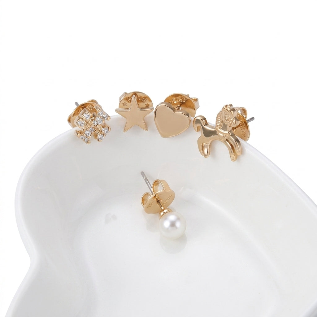 A set of five gold-tone stud earrings displayed on a white ceramic dish against a white background. The designs include a flower with clear crystals, a star, a heart, a small dog, and a single pearl stud.