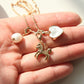 A gold-tone charm necklace with a horse, heart, and pearl bead, held in a person's hand.
