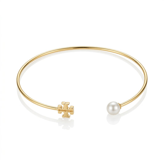 A gold open cuff bangle bracelet featuring a small gold cross charm on one end and a single white pearl on the other, displayed on a clean white background.