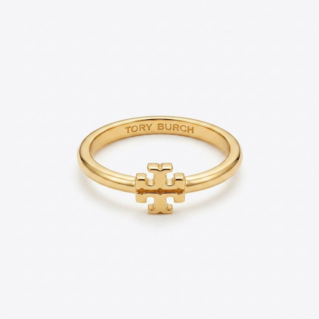 A gold ring featuring a small interlocking T logo charm on the front, with 'TORY BURCH' engraved inside the band, set against a clean white background.