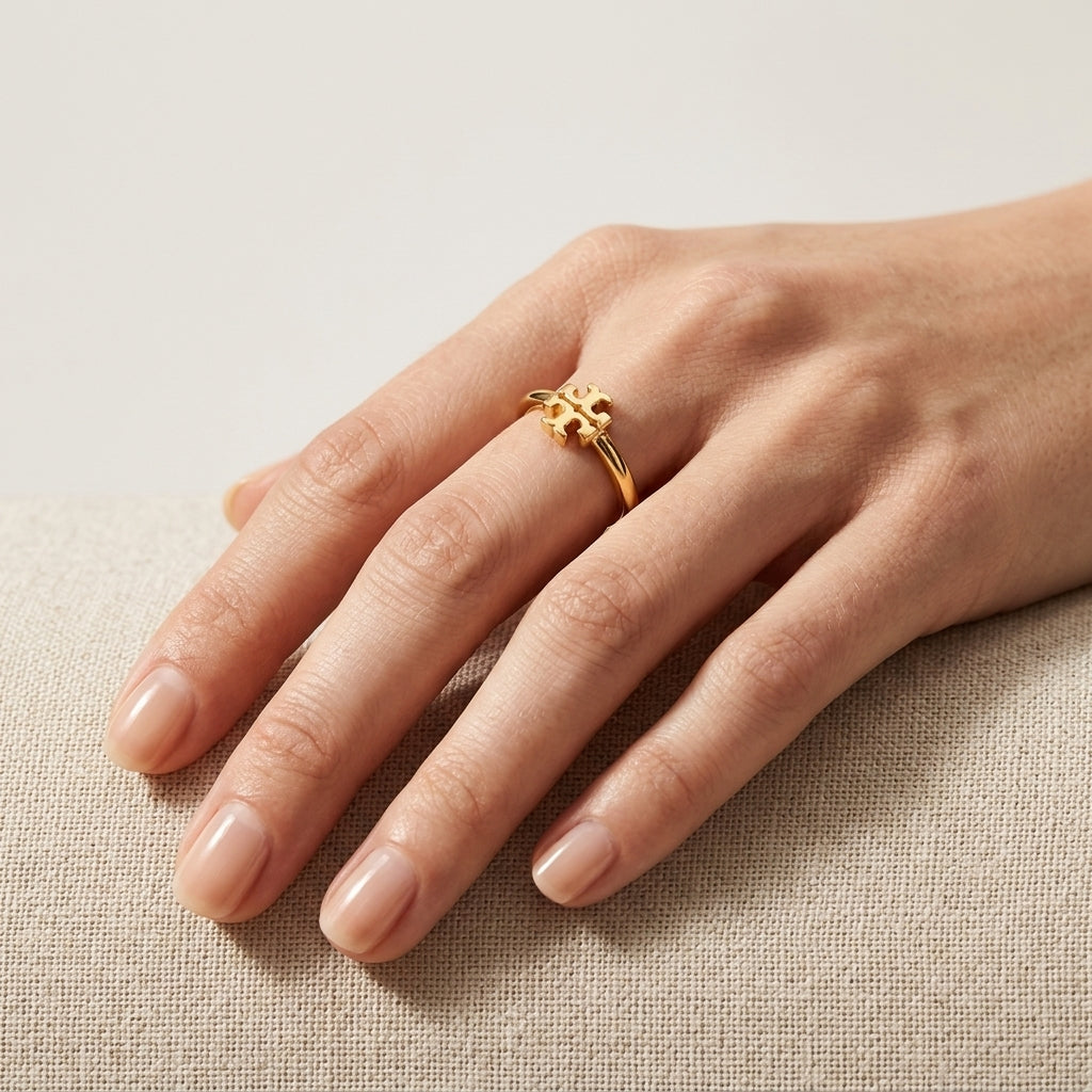 A delicate gold ring with a small sculpted floral or starburst motif worn on a person's ring finger, resting on a textured beige fabric surface.