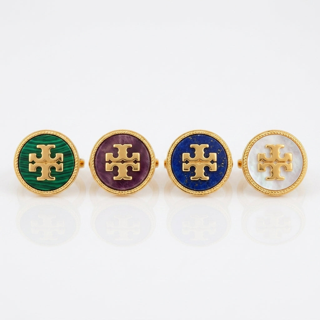 Four oval gold-tone cufflinks with enamel inserts in green, purple, blue, and white, each featuring a raised gold cross logo, arranged on a white reflective surface.