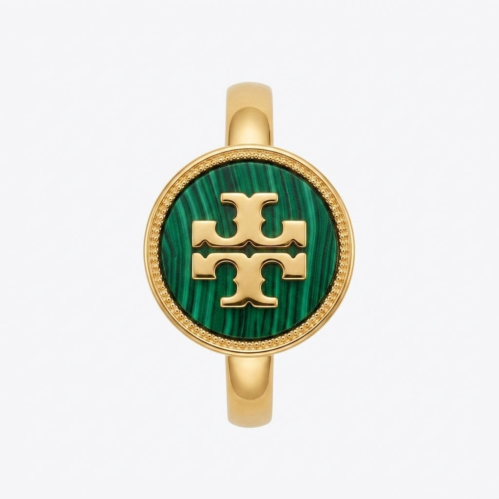 A gold ring featuring a circular green malachite inlay with a gold interlocking T logo in the center, representing the Tory Burch logo, set against a light gray background.