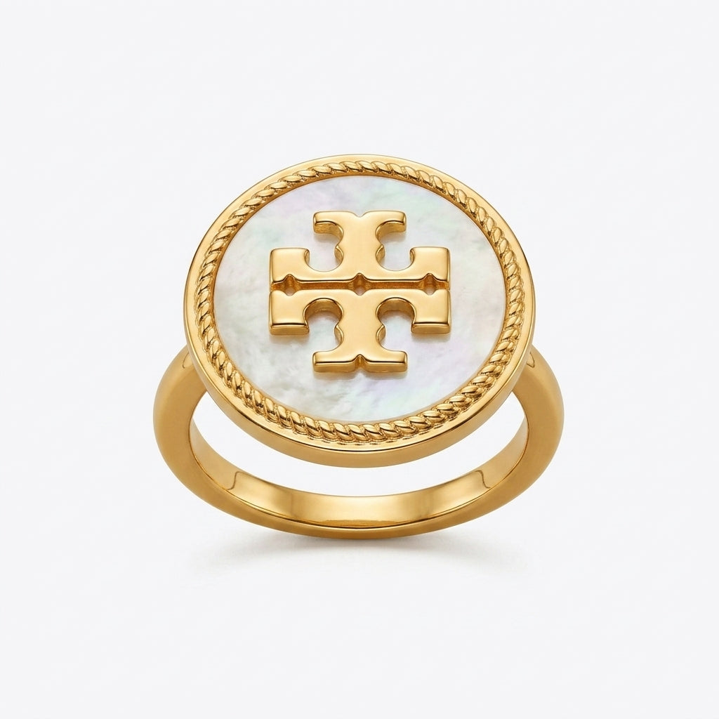 A gold ring featuring a round white mother-of-pearl inlay with a raised gold monogram logo in the center, set against a light gray background.