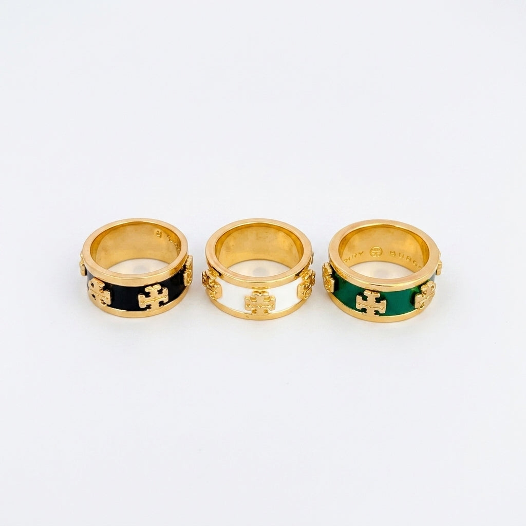 Three gold rings with interlocking cross motifs and colored enamel bands, displayed side by side on a light gray background.
