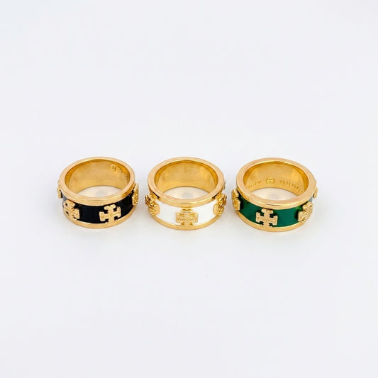Three gold rings with interlocking cross motifs and colored enamel bands, displayed side by side on a light gray background.