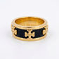 A gold ring with a black enamel center and raised gold logo details, photographed on a plain white background.
