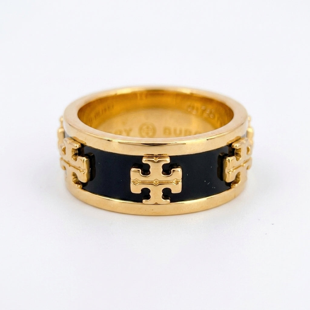 A gold ring with a black enamel center and raised gold logo details, photographed on a plain white background.
