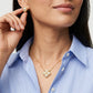 A close-up lifestyle shot of a model wearing a gold flower-shaped pearl necklace and matching pearl stud earring, paired with a light blue striped button-down shirt.