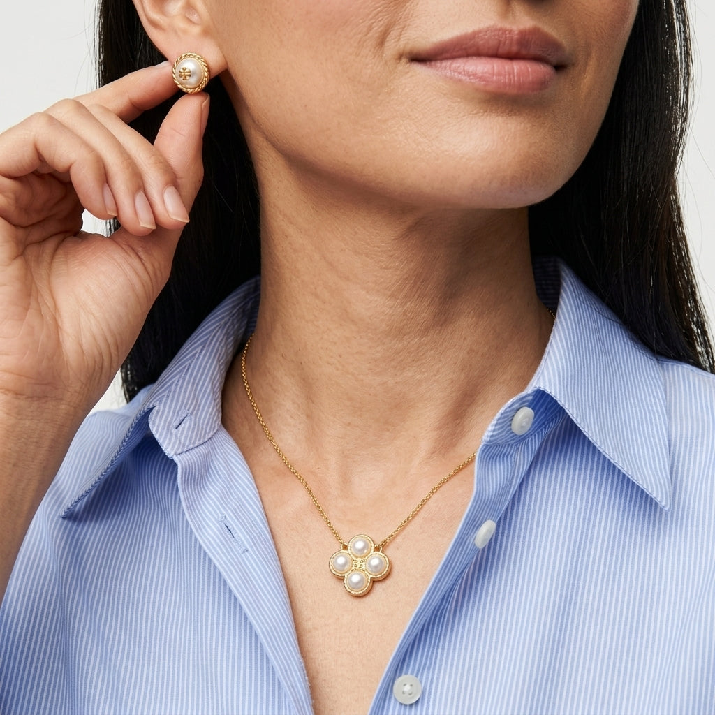 A close-up lifestyle shot of a model wearing a gold flower-shaped pearl necklace and matching pearl stud earring, paired with a light blue striped button-down shirt.