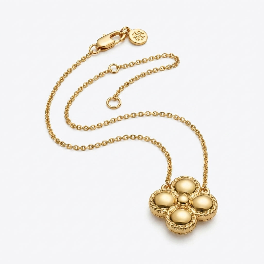 A gold-tone chain necklace with a textured, five-petal flower-shaped pendant, displayed on a clean white background. A small circular brand tag is attached to the clasp.