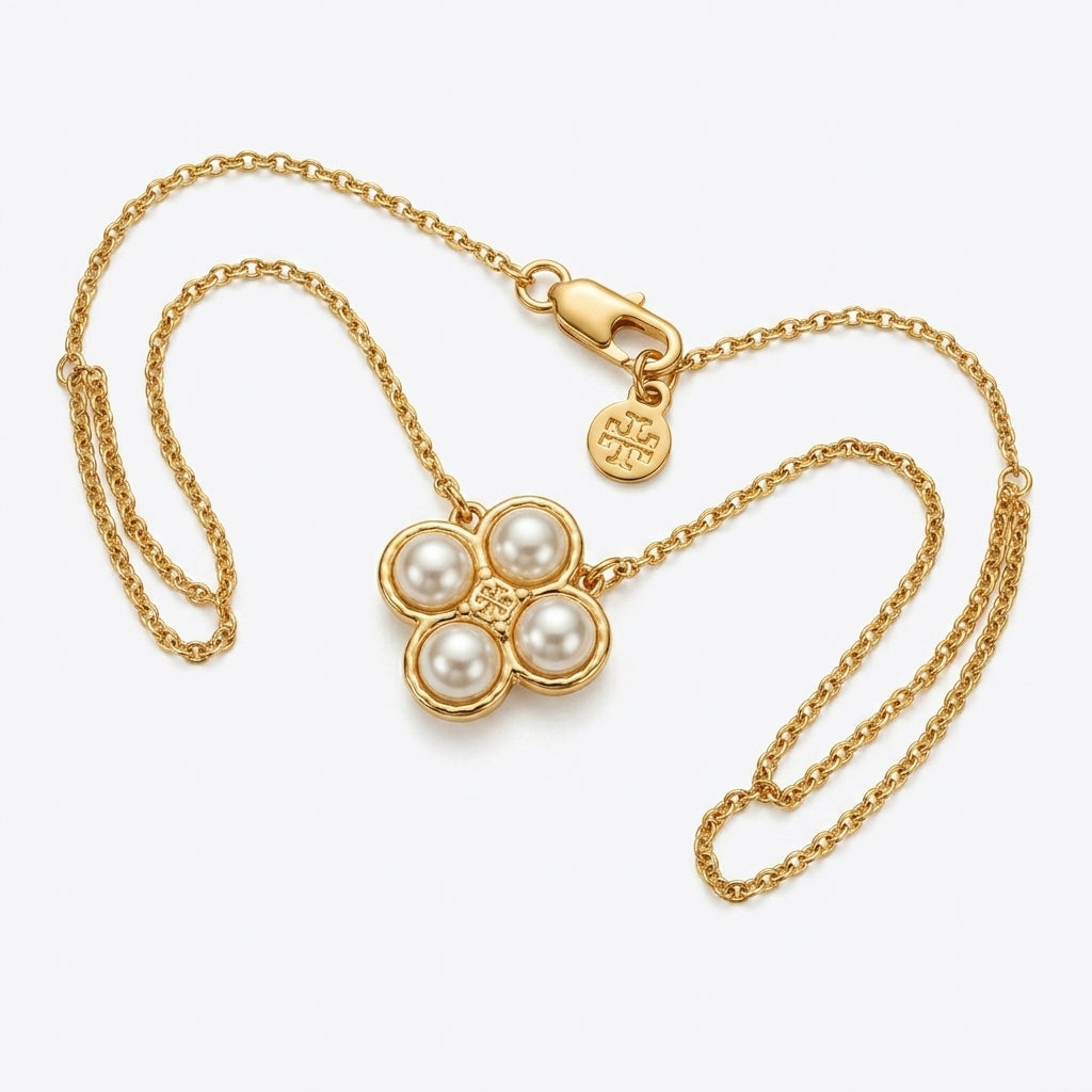 A gold chain necklace featuring a four-petal flower pendant with four white pearls and a small central gold heart, displayed on a light gray background.