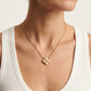 A close-up of a model wearing a delicate gold chain necklace with a small flower-like pendant made of five white pearls, styled with a white ribbed tank top.