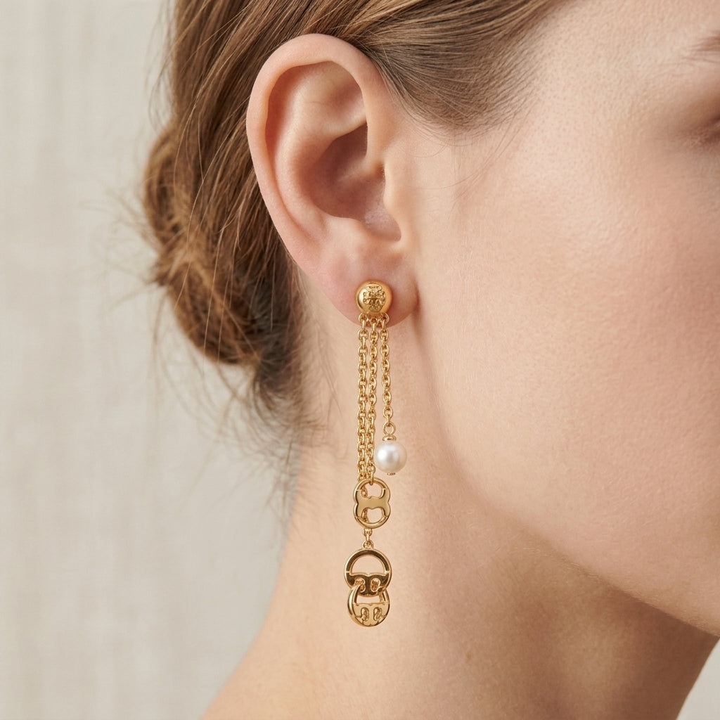 A close-up of a model's ear wearing a gold dangle earring with a small white pearl and a decorative lock charm.
