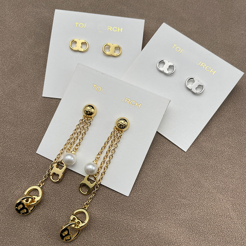 Both earrings displayed hanging freely against a dark, solid background, clearly showing the layered chains, pearls, and logo stud.