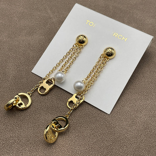 Both earrings displayed hanging freely against a dark, solid background, clearly showing the layered chains, pearls, and logo stud.