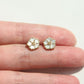 Flower-shaped earrings held between two fingers on a light background