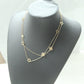 A gold double-strand necklace with small clover-like motifs and openwork diamond details, displayed on a dark gray jewelry bust against a light background.