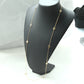 A delicate gold chain necklace with small geometric and floral motifs, displayed on a black jewelry bust against a light gray background.