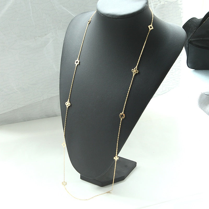 A delicate gold chain necklace with small geometric and floral motifs, displayed on a black jewelry bust against a light gray background.